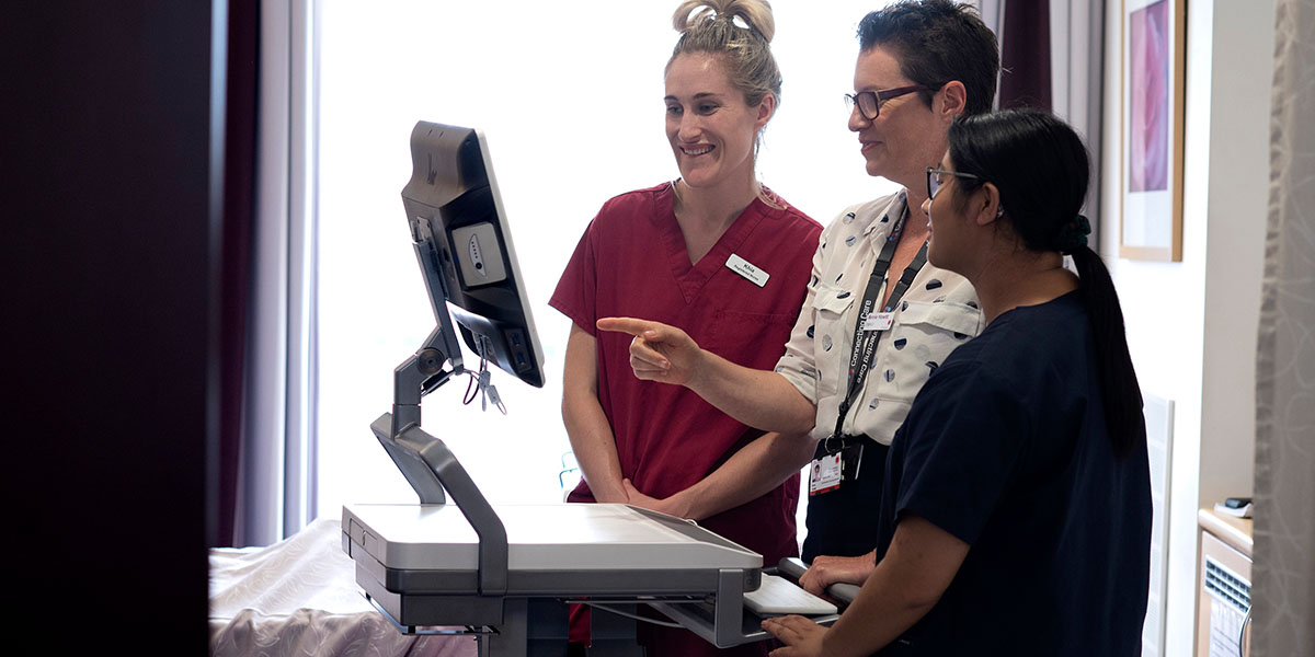 Three staff check a patient monitor screen