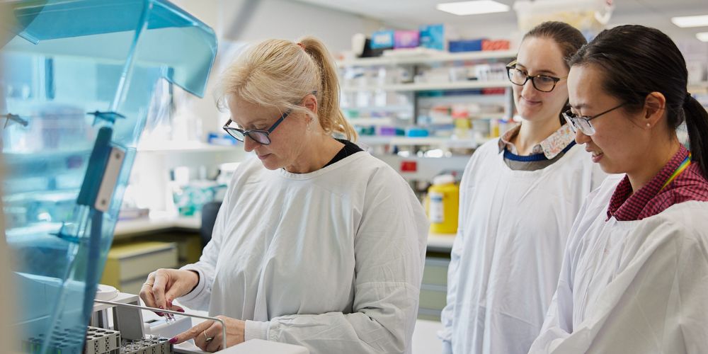 Three female researchers wearing white scrubs working in the Women's lab. 