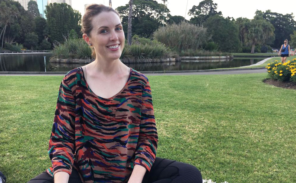 Woman sits cross legged on the grass in a park.